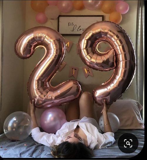 a woman laying on top of a bed next to balloons in the shape of the number twenty