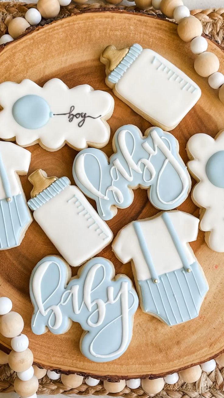 cookies decorated with blue and white icing on a wooden platter that says baby