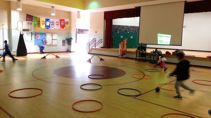 children are playing with hoop rings on the floor in an indoor gym area at school