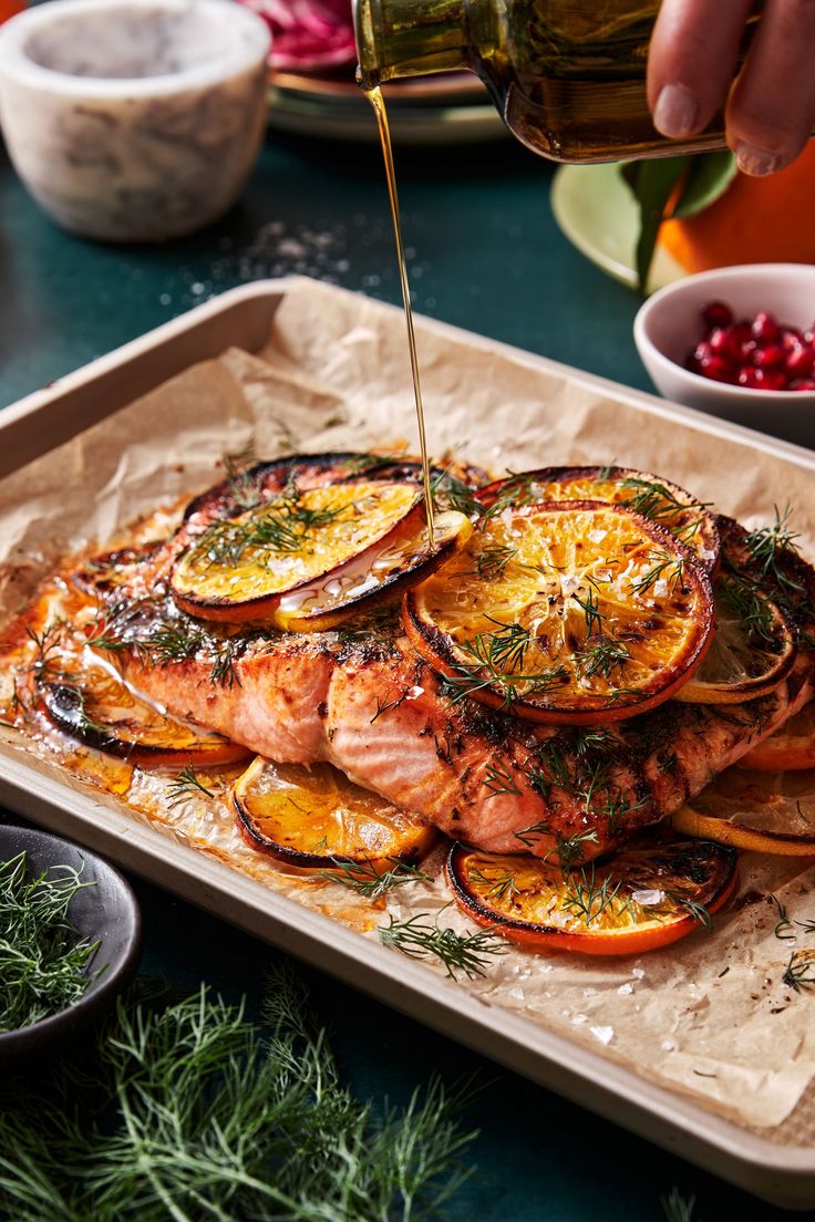 someone is pouring olive oil on the salmon with orange slices and onions in a pan