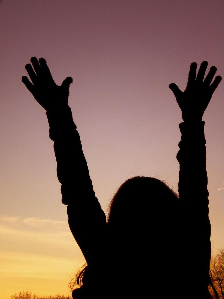 the silhouette of a woman with her hands up in the air at sunset or dawn