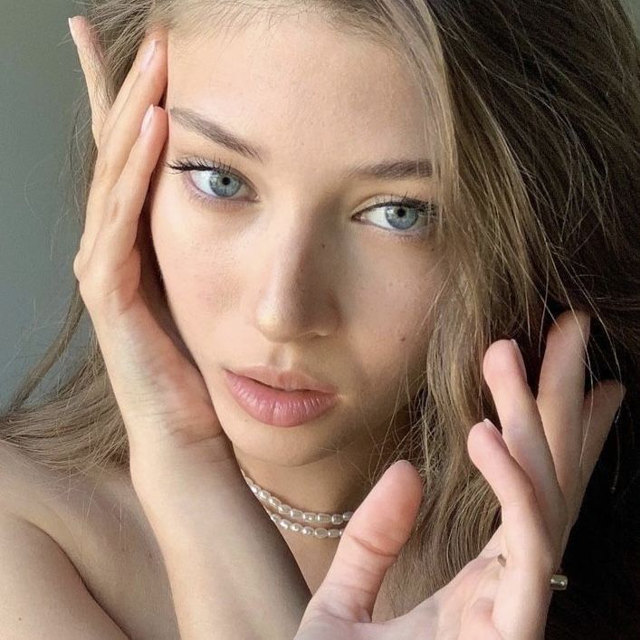 a beautiful young woman with blue eyes posing for the camera and holding her hand to her face