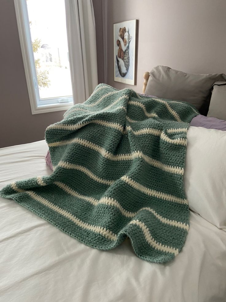 a green and white blanket sitting on top of a bed next to a window in a bedroom