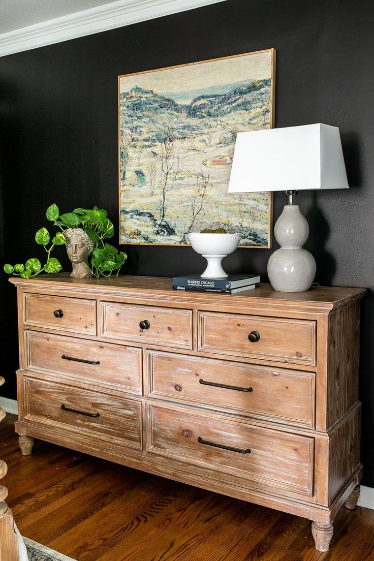 a wooden dresser with two lamps and a painting on the wall