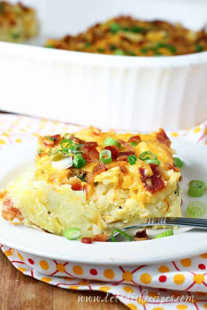 a white plate topped with a casserole covered in bacon and green onions next to a baking dish