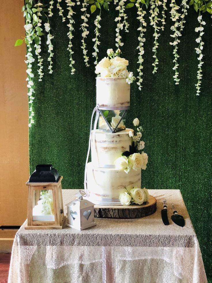 a tall white cake sitting on top of a table next to a green wall covered in flowers