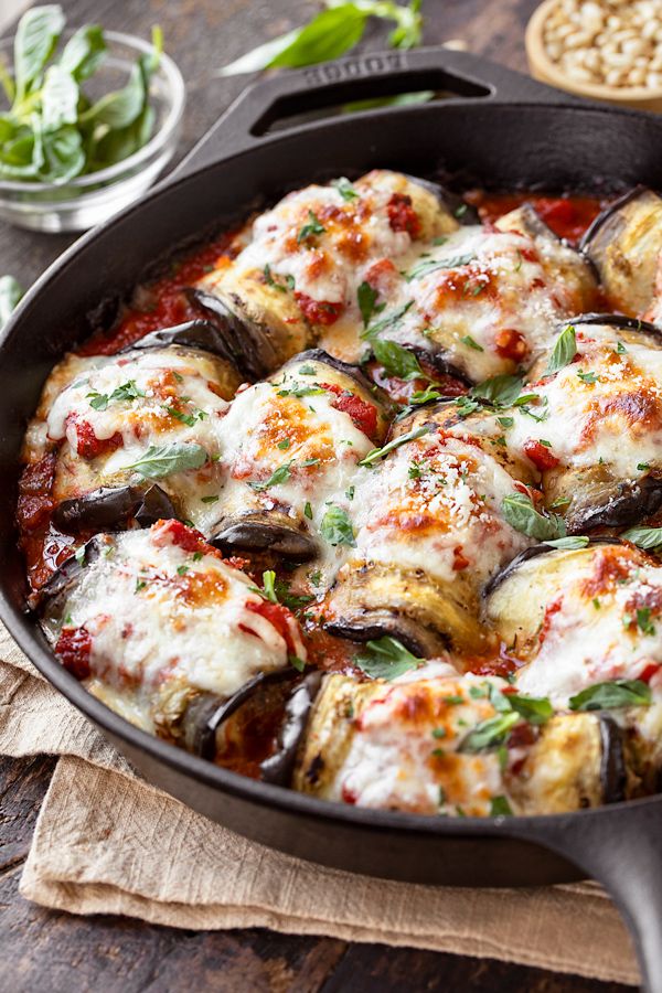 a skillet filled with eggplant covered in cheese and sauce on top of a wooden table