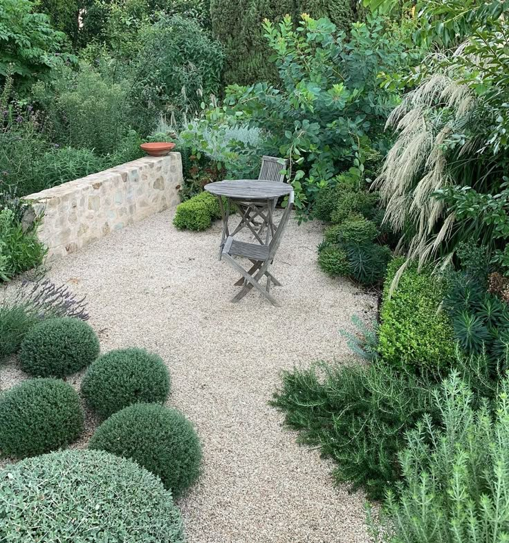 a table and chair in a garden with graveled path leading to the back yard