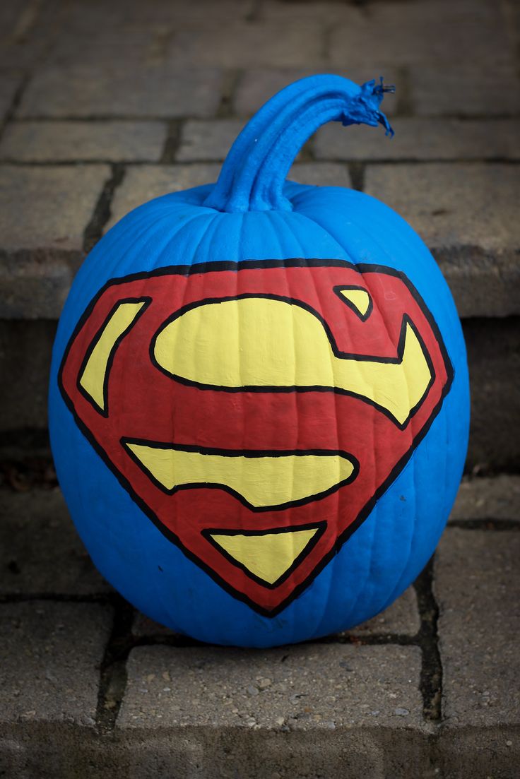 a blue pumpkin with a superman symbol painted on it's side sitting on the ground