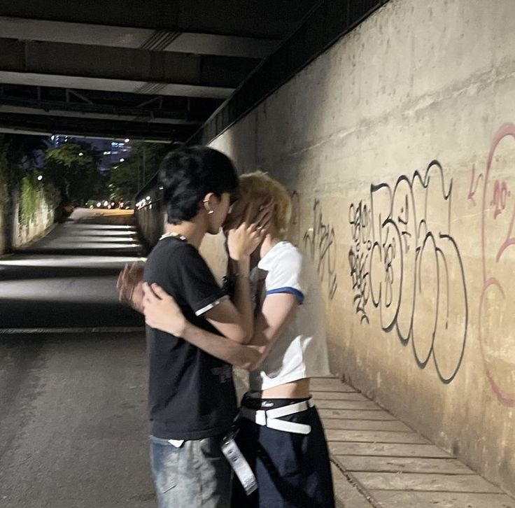 two people standing next to each other in front of a wall with graffiti on it