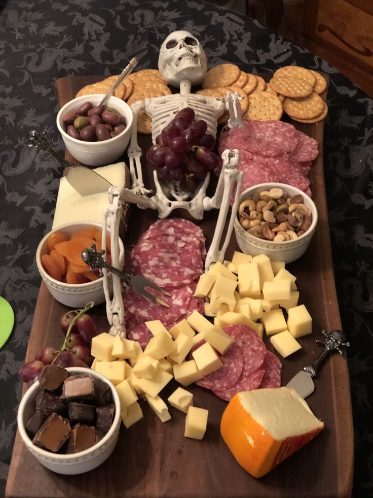 a wooden cutting board topped with meat and cheeses next to bowls of crackers