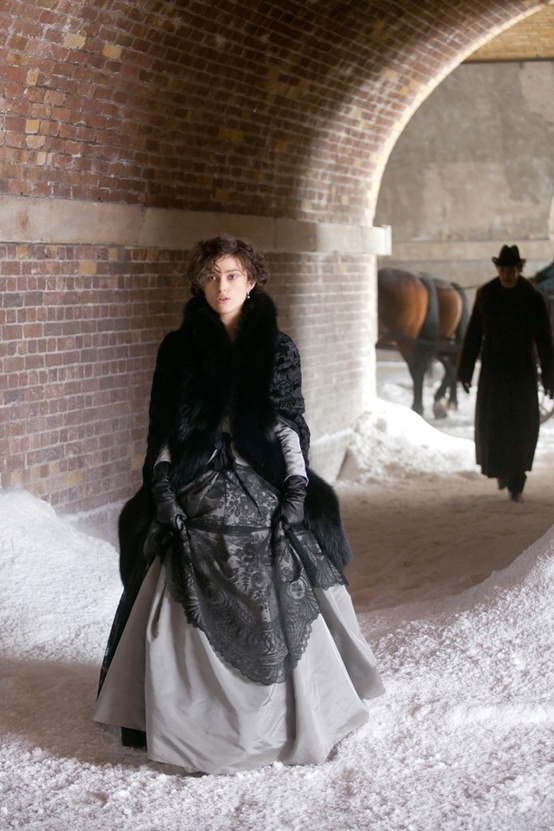 a woman is walking in the snow with two horses behind her and another man standing next to her