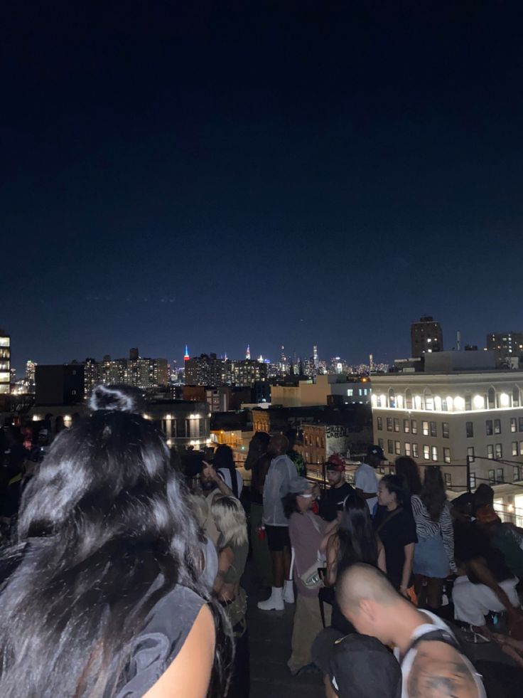 a group of people standing on top of a roof at night with city lights in the background