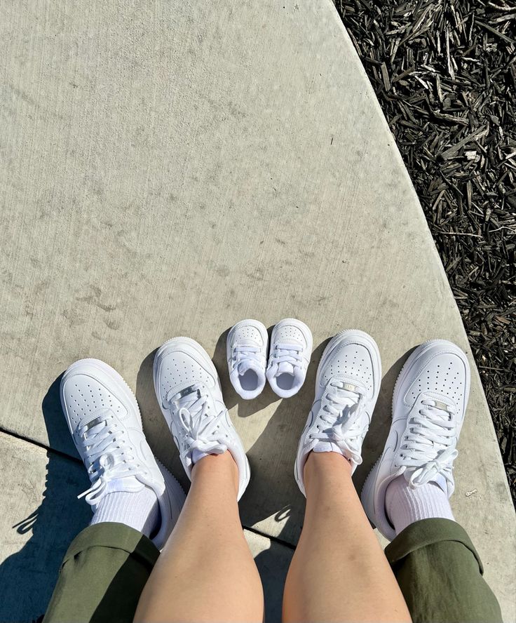 the legs and feet of a person wearing white tennis shoes on a concrete surface with grass in the background