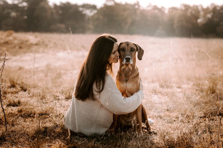 a woman is sitting in the grass with her dog and kissing her face on his chest