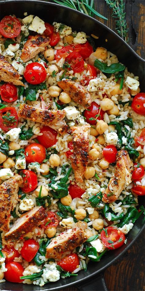 a skillet filled with chicken, chickpeas, tomatoes and spinach on top of a wooden table