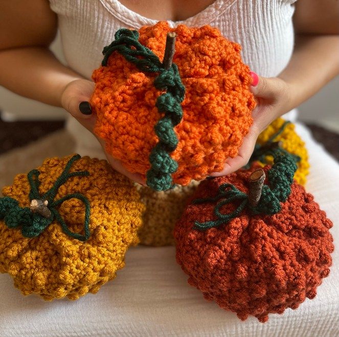 three crocheted pumpkins sitting on top of a white blanket with one being held by a woman