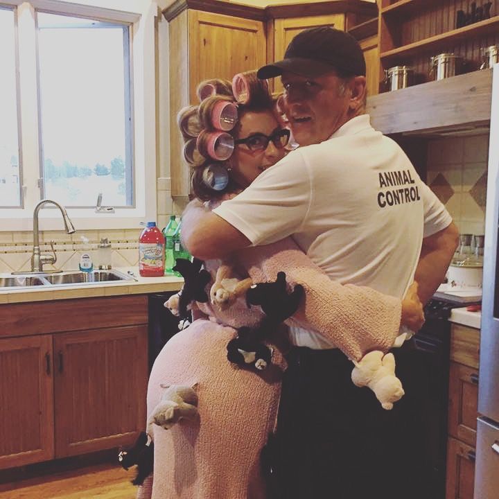 a man and woman hug in the kitchen with stuffed animals on their backs while they're dressed for halloween