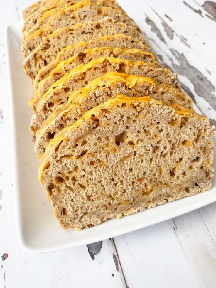 sliced loaf of bread on a white platter with orange sauce and cheddar