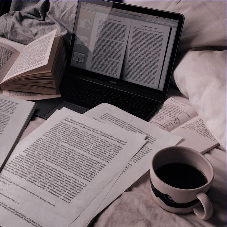 an open laptop computer sitting on top of a bed next to two books and a cup of coffee