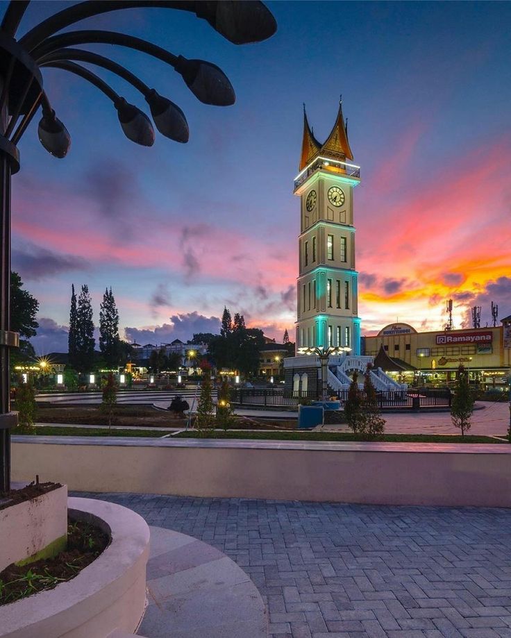 a clock tower lit up at night with the sun setting in the sky behind it