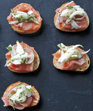 several open faced sandwiches with meat and cheese on them sitting on a black surface, ready to be eaten