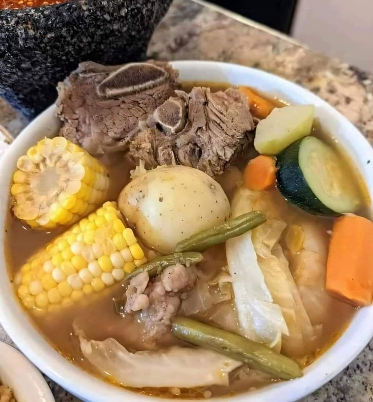 a bowl filled with meat, vegetables and corn on the cob next to another bowl