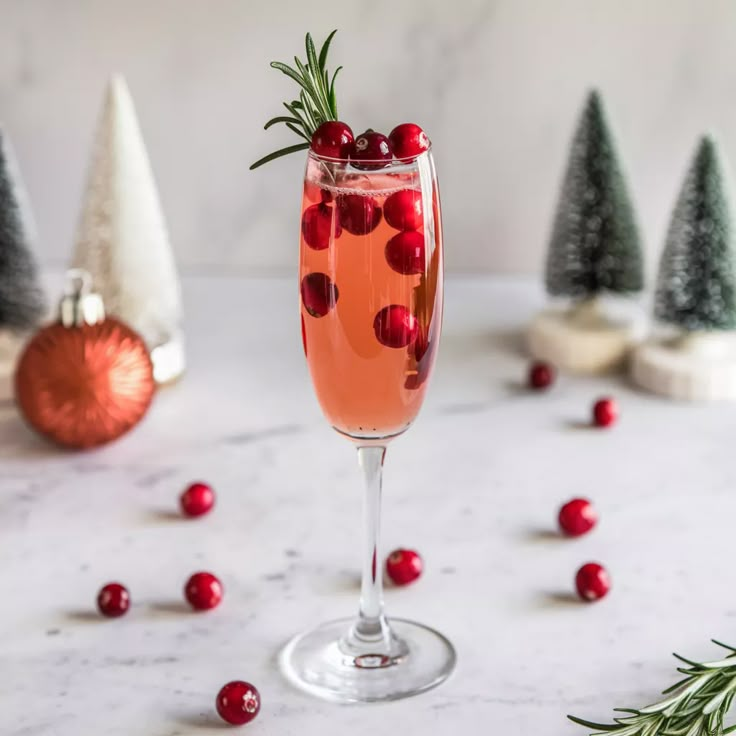 a glass filled with wine and garnished with cranberries next to christmas trees