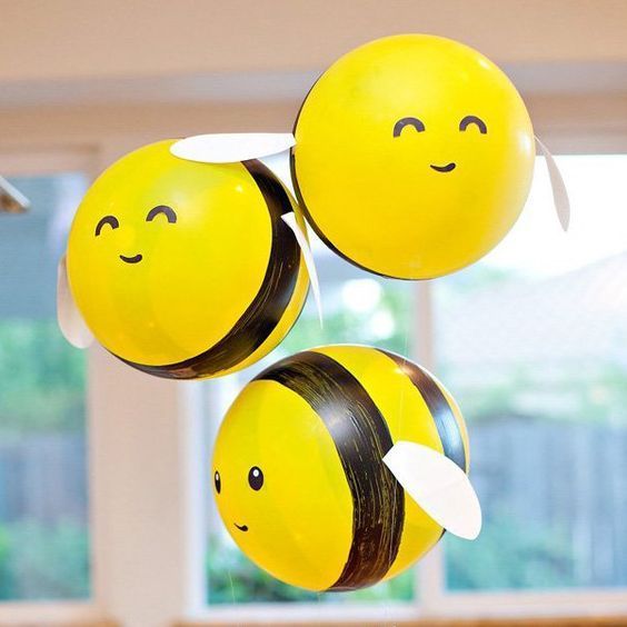 three yellow balloons with faces hanging from them in the shape of bee's heads