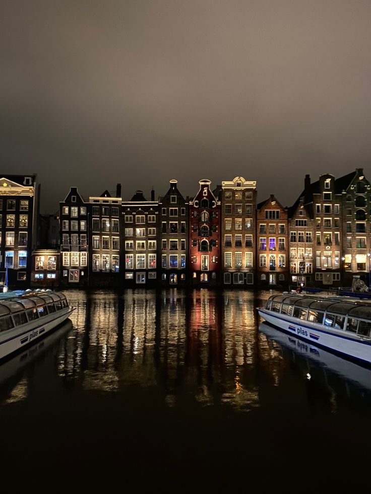 several boats are docked on the water in front of some buildings and lights at night