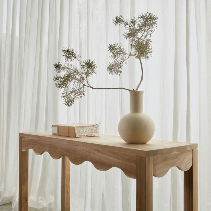 a white vase sitting on top of a wooden table next to a book and plant