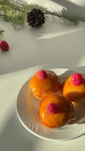 three donuts on a plate with raspberries and pine cones in the background