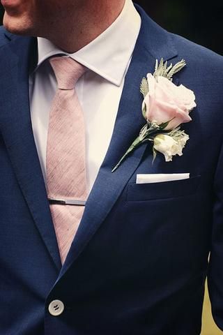 a man wearing a blue suit and pink tie with a white flower on his lapel