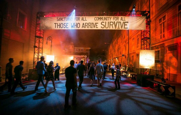 a group of people standing around in front of an arch with a sign that says those who arrive survive