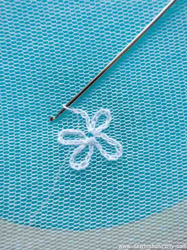 the needle is being used to make an embroidered flower on a piece of mesh fabric