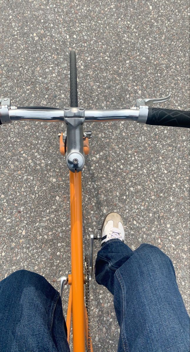 the legs of a person riding a bike on asphalt with blue jeans and white shoes