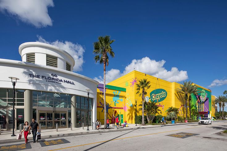 two people are walking down the street in front of a shopping center with palm trees