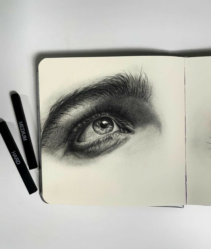 an open notebook with two pencils next to it and a drawing of an eye