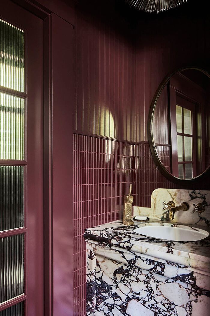 a bathroom with red walls and marble counter tops, along with a round mirror on the wall