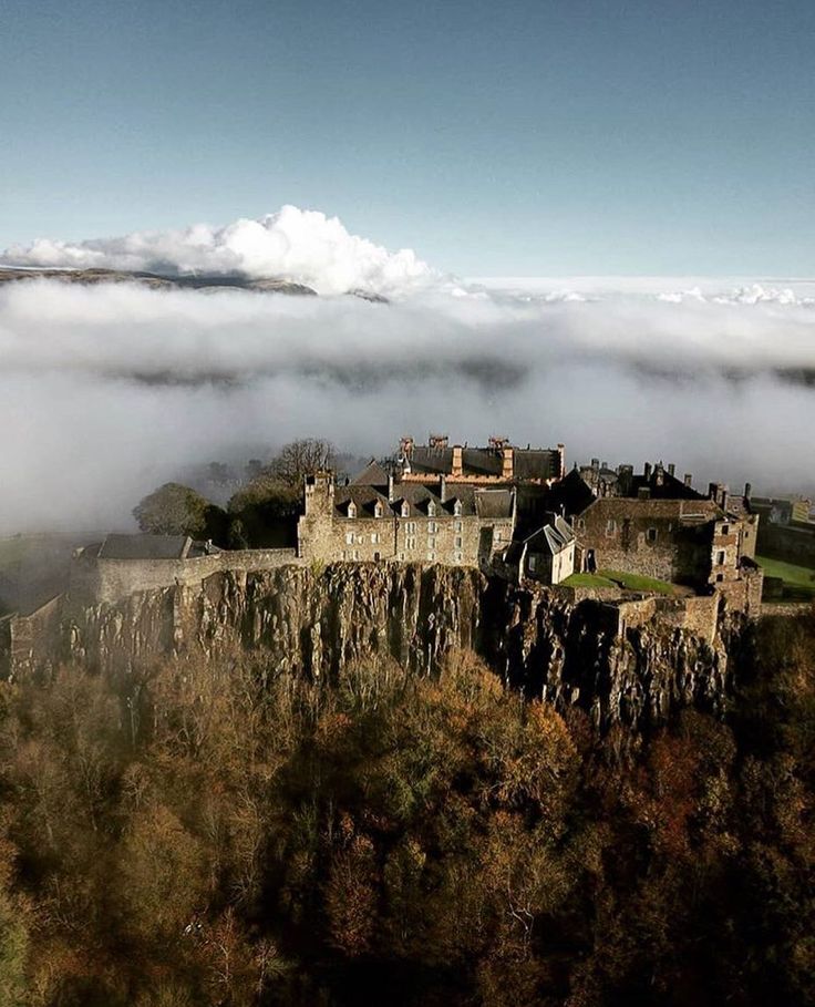 an old castle on top of a cliff in the middle of foggy skies and low lying clouds