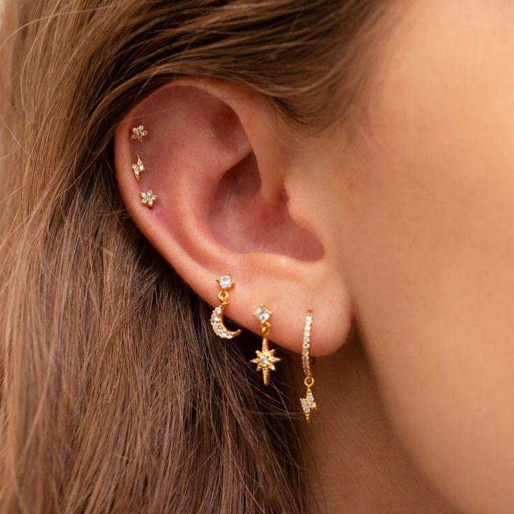 a woman's ear is adorned with gold stars and moon earrings