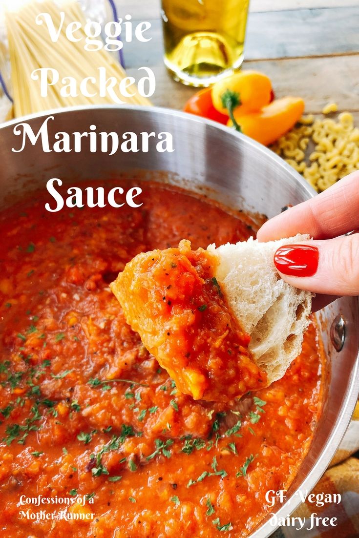 a hand holding a piece of bread over a bowl of marinara sauce