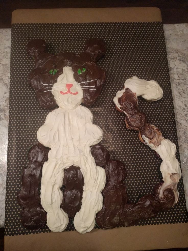 a cake shaped like a cat sitting on top of a counter next to some cookies