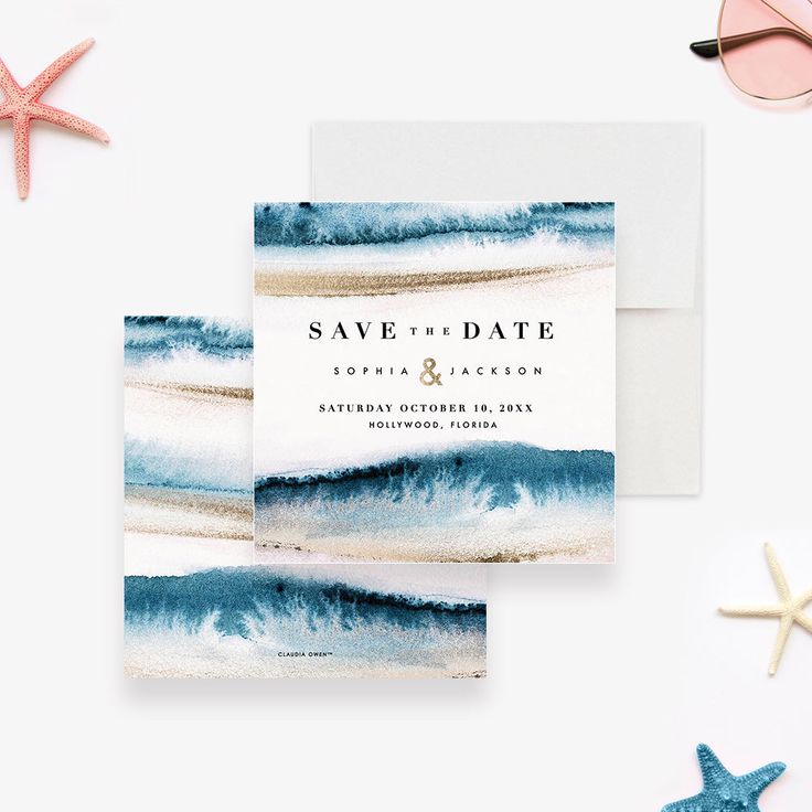 save the date cards with blue watercolor waves and starfish on white paper next to them