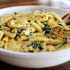 a white bowl filled with pasta and spinach on top of a wooden table next to a cup