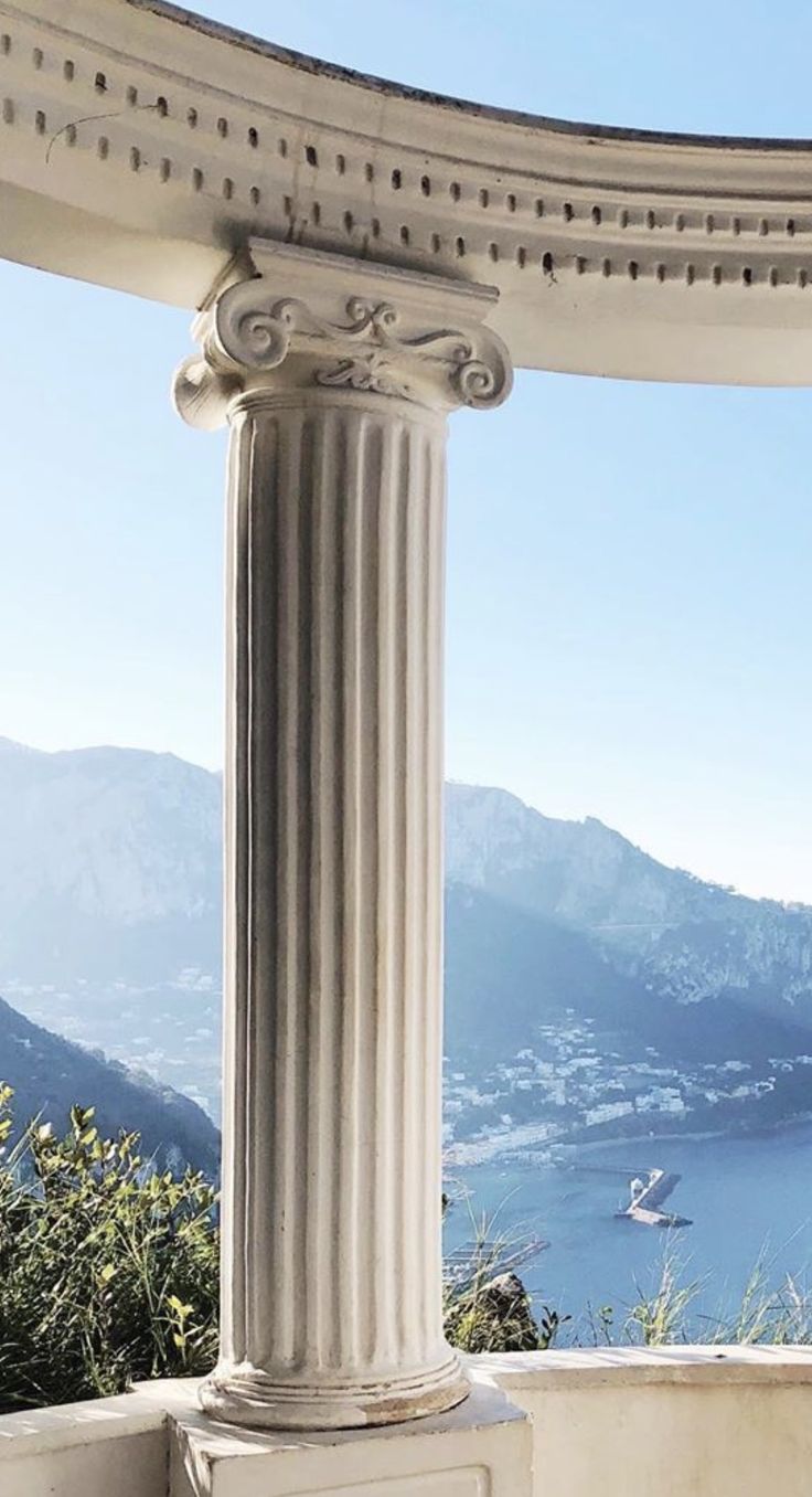 an ornate column stands in front of a view of the ocean and mountains from a gazebo