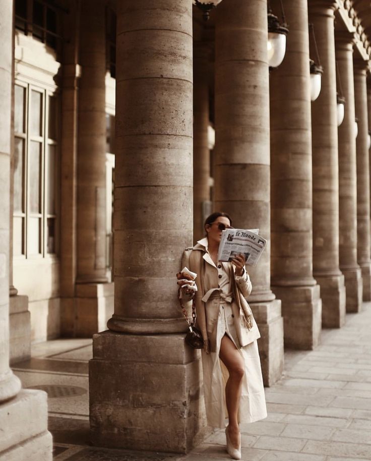 a woman standing next to columns reading a newspaper