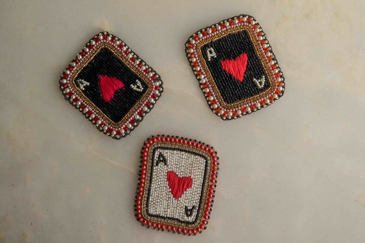 three pieces of beaded cloth with red hearts and playing cards on them sitting on a white surface