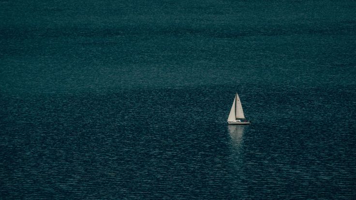 a lone sailboat floating in the middle of the ocean with dark blue water behind it