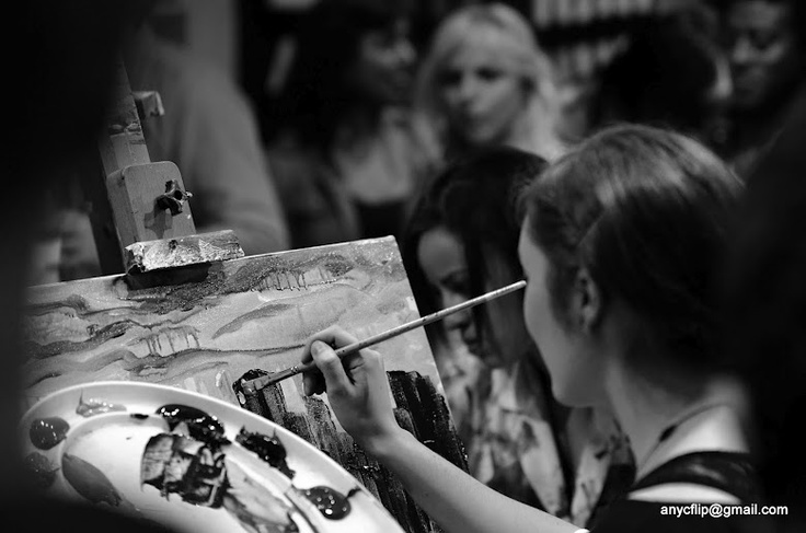 a woman is painting on an easel while others look on